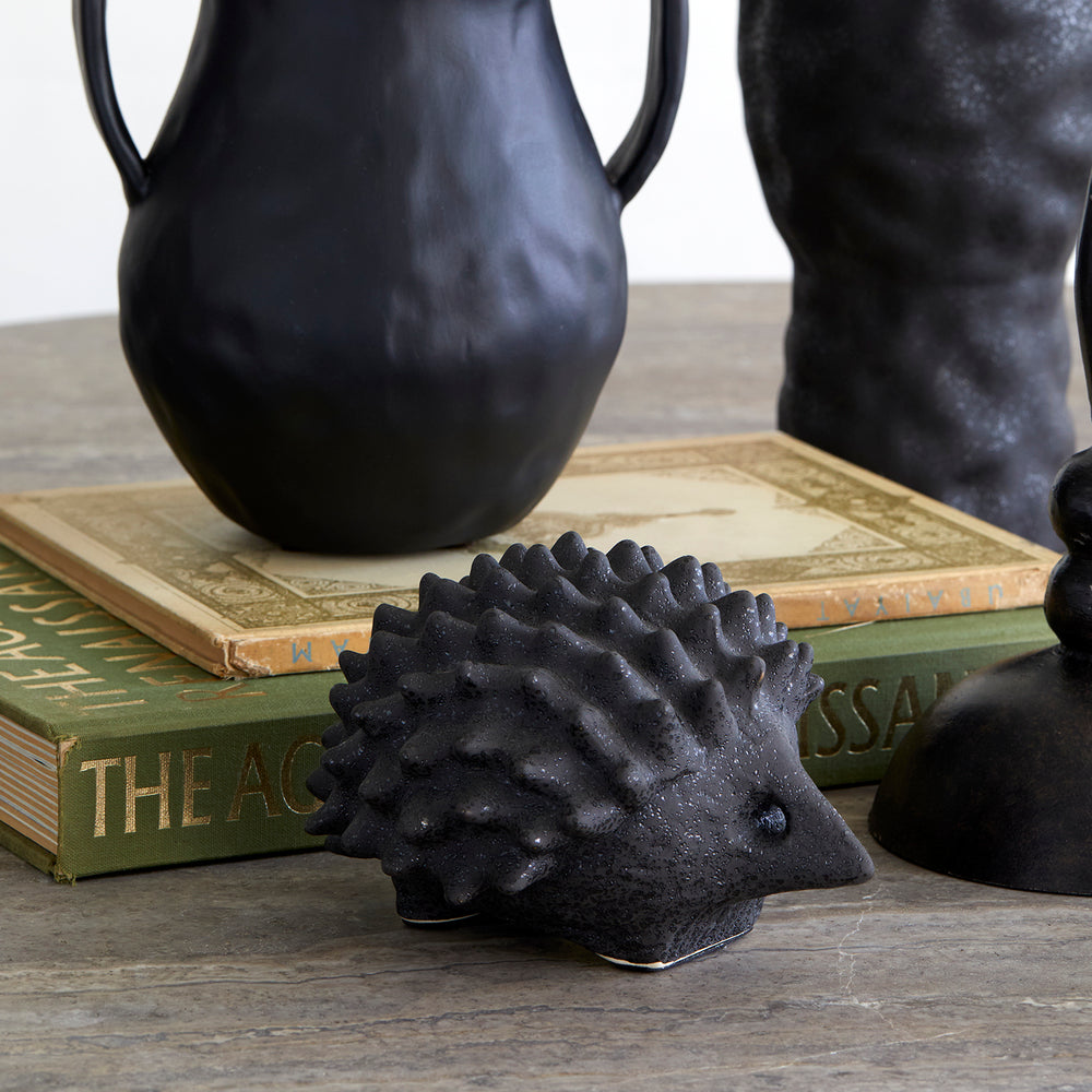 Lemieux et Cie Porcupine in textured black glaze, sculptural ceramic accent piece, styled on weathered wood surface with vintage books and dark vessels.