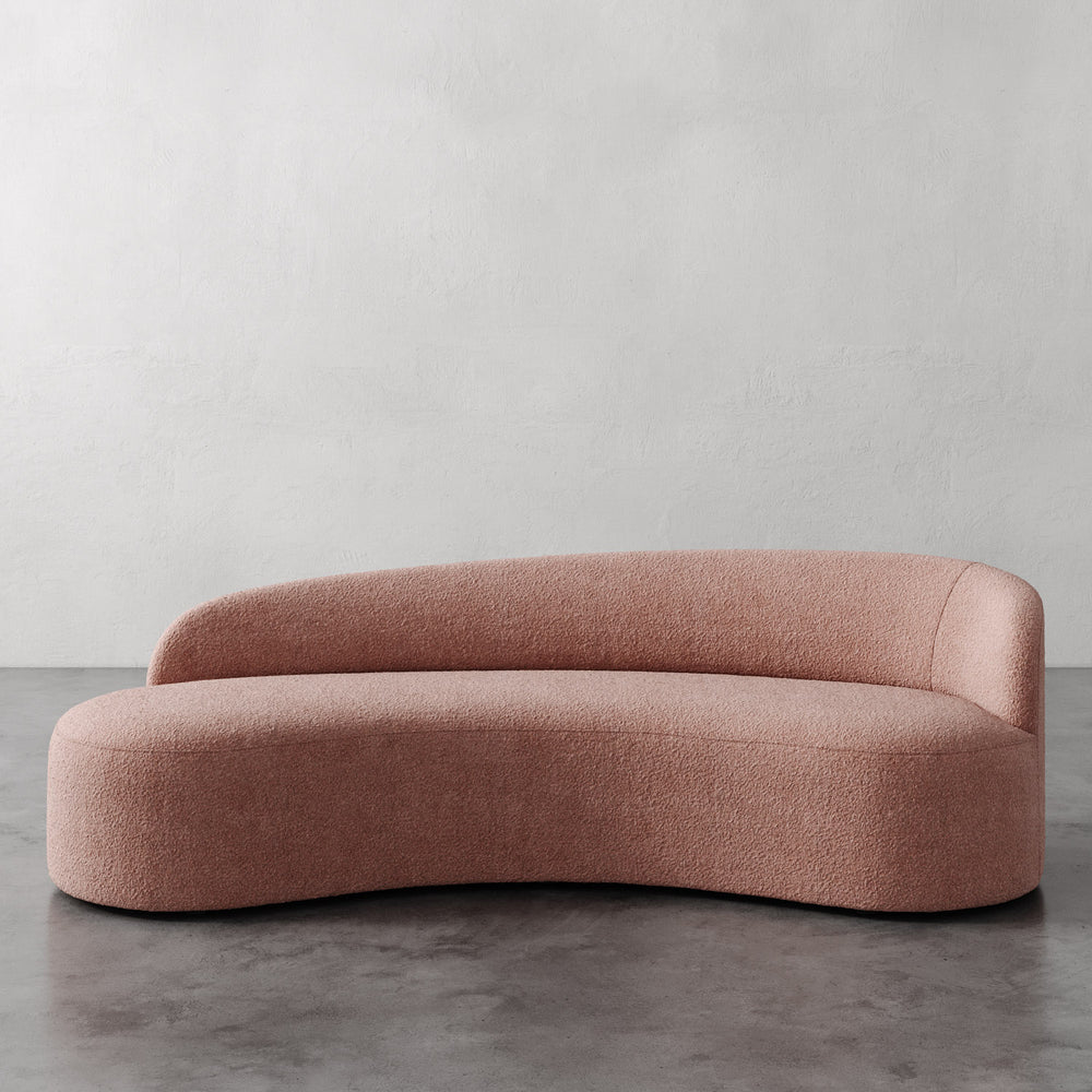 Lemieux et Cie Colette Right Arm Sofa in blush bouclé, sculptural curved sofa with organic asymmetric form, shown on polished concrete floor against white wall.