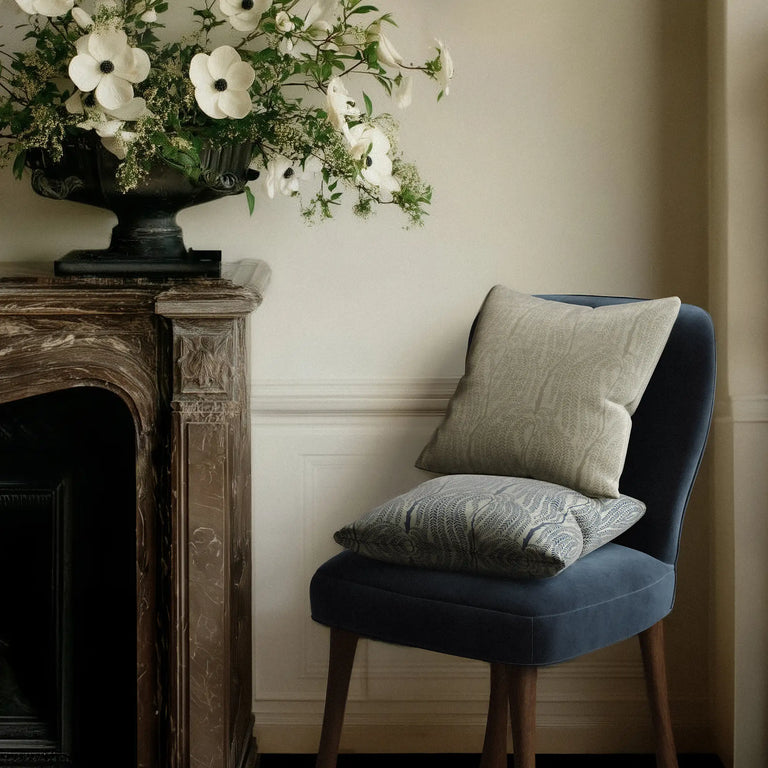 Blue velvet Rozette chair with 2 Linen accent pillows in the cascading willow botanical pattern in neutral and indigo next to a marble mantle with flowers