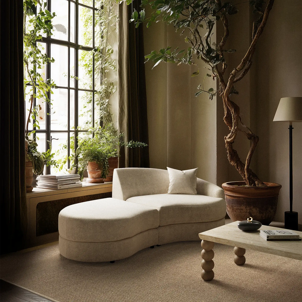 Lemieux et Cie Rulmann Left Ottoman in cream, organic curved chaise sectional in a light-filled room with steel-framed windows and greenery.