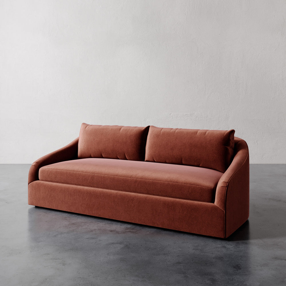 Lemieux et Cie Rousseau Sofa in warm terracotta upholstery, sofa with curved arms and bench cushion, shown on polished concrete floor against white walls.