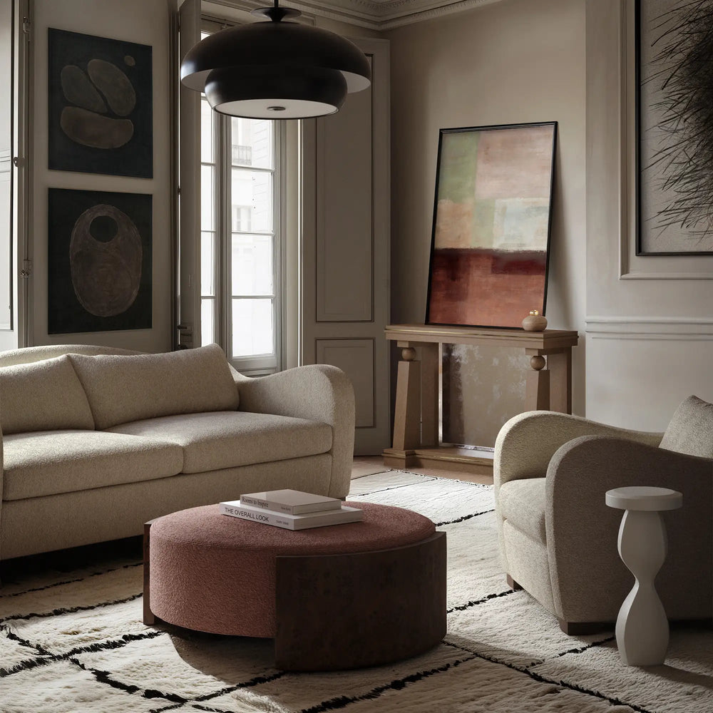 Lemieux et Cie Benoit Coffee Table Ottoman in wire-brushed oak with rounded upholstered top, styled in a sitting room with neutral walls, wood floors, and soft daylight.