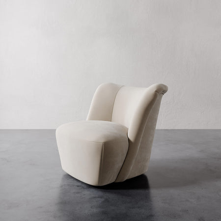 Lemieux et Cie Aurélie Swivel Chair in ivory, sculptural rounded chair with curved back, shown on dark concrete floor against white textured wall.
