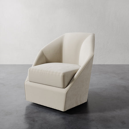 Lemieux et Cie Bijou Swivel Chair in ivory, sculptural curved-back chair with tailored skirted base, shown on dark concrete floor.