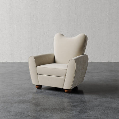 Lemieux et Cie Danielle Chair in pale neutral upholstery, sculptural wingback armchair with curved silhouette and rounded feet, on concrete floor against plaster wall.