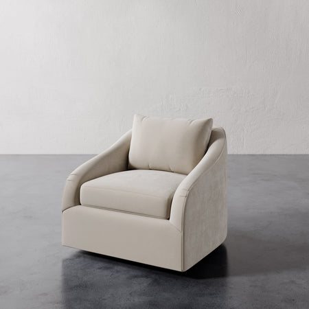 Lemieux et Cie Rousseau Swivel Chair in warm neutral upholstery, curved-arm lounge chair on concrete floor against textured plaster walls.