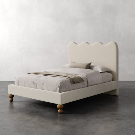 Lemieux et Cie Celine Bed, upholstered bed with scalloped headboard and turned legs, dressed in neutral linens on polished concrete floor.