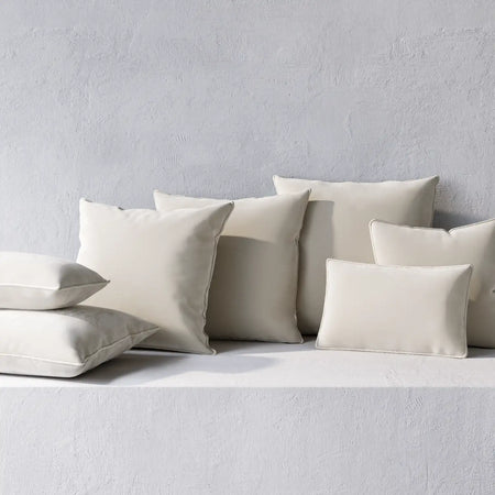 Lemieux et Cie Throw Pillows in cream with welted edges, pillows arranged on textured plaster surface in soft natural light.