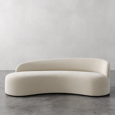 Lemieux et Cie Colette Right Arm Sofa in ivory, sculptural curved sofa with organic asymmetric form, shown on polished concrete floor against neutral plaster walls.
