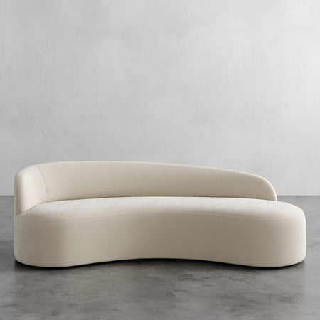 Lemieux et Cie Colette Left Arm Sofa in ivory upholstery, sculptural curved sofa with organic silhouette, shown on concrete floor against neutral walls.