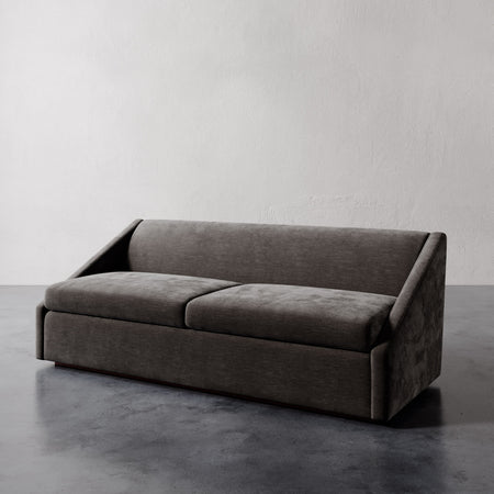 Lemieux et Cie Fontaine Sofa with architectural silhouette and angled arms, upholstered sofa shown on polished concrete floor against textured plaster walls.