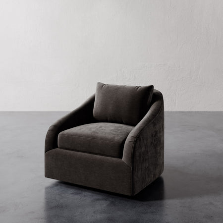 Lemieux et Cie Rousseau Swivel Chair in charcoal upholstery, sculptural lounge chair with sloped arms, shown on concrete floor against textured plaster wall