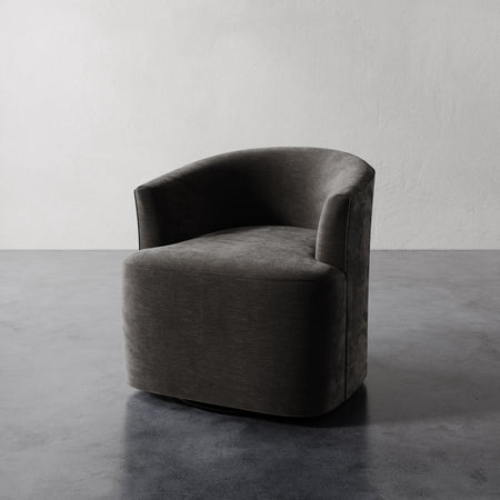 Lemieux et Cie Garnier Swivel Chair in charcoal upholstery, sculptural rounded form, shown on polished concrete floor against white textured wall.