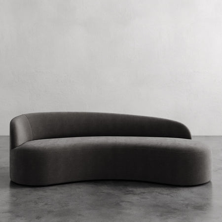 Lemieux et Cie Colette Left Arm Sofa in charcoal, curved asymmetric sofa with organic sculptural silhouette on concrete floor against textured plaster wall.