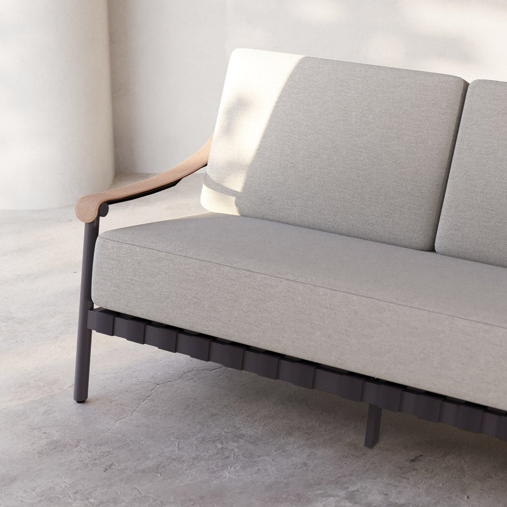 Lemieux et Cie Hudson Dining Arm Chair in warm grey upholstery, low-profile lounge chair with curved arms, shown on concrete floor against white walls in soft daylight.