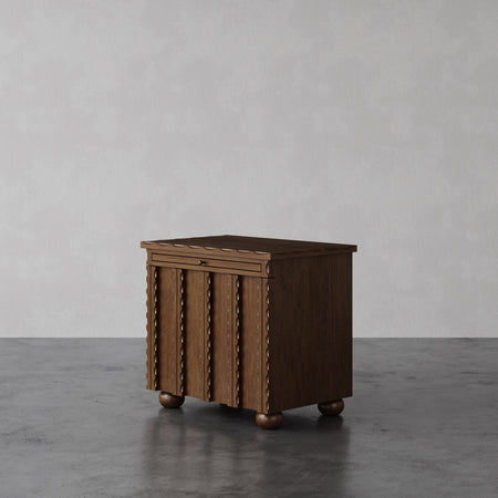 Lemieux et Cie Marchand Nightstand in walnut oak with scalloped detailing and textured doors, cabinet on ball feet shown on polished concrete floor.