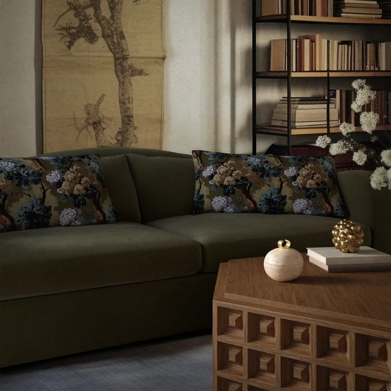 Lemieux et Cie Folie Floral Velvet Pillow in muted olive green with botanical motif, styled on sectional sofa in sitting room with dark bookshelf and artwork.