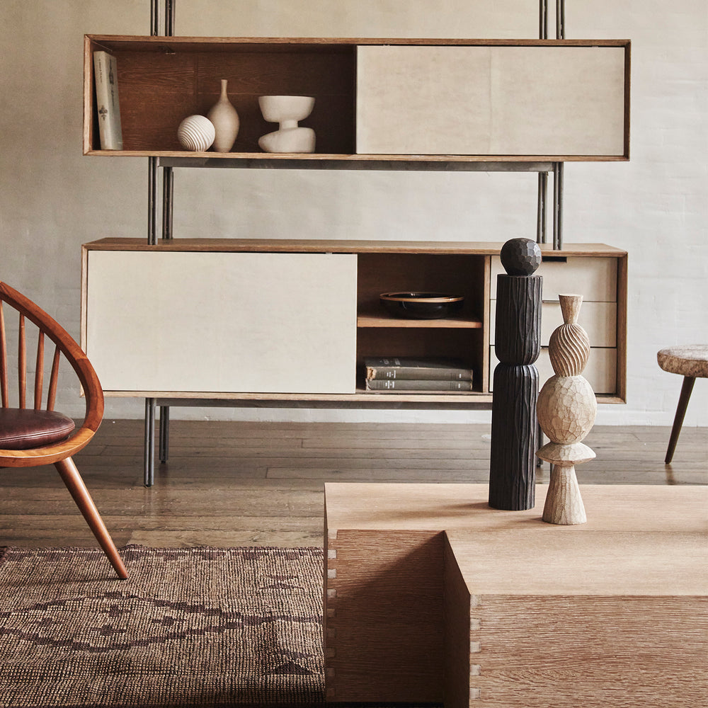 Lemieux et Cie Chapon Pillar, sculptural wooden decorative object with layered geometric forms, styled atop a low table near shelving in a sitting room with wood floors and neutral walls.