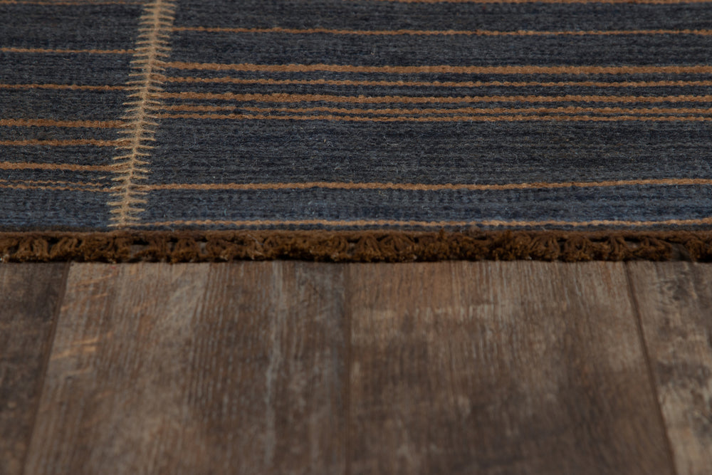 Lemieux et Cie Moghar rug in charcoal and warm brown handwoven jute flatweave, detail of organic striped pattern and raw edge on weathered wood flooring.