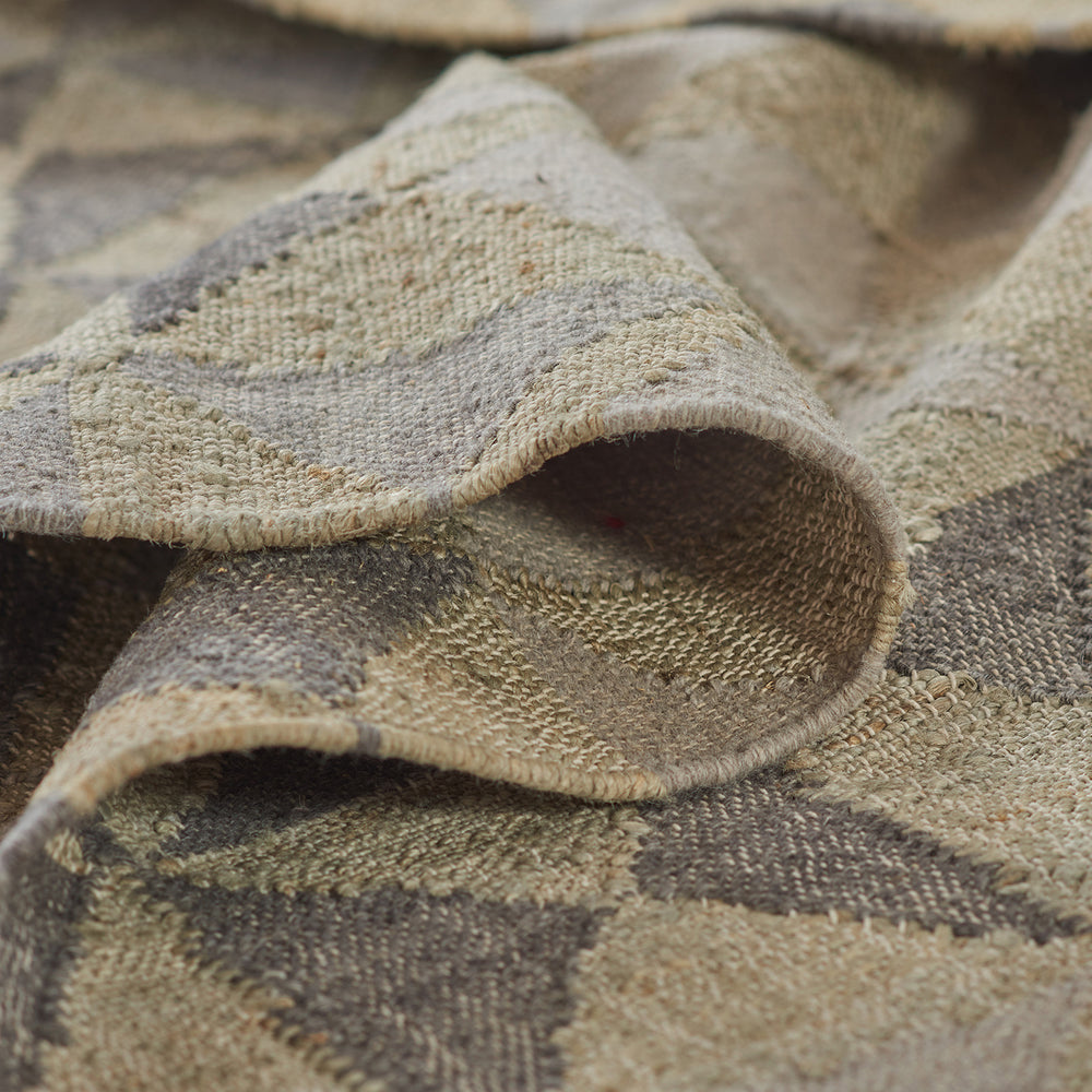 Lemieux et Cie handwoven rug in neutral tones with geometric pattern, textile swatch shown folded to reveal textured weave and backing.