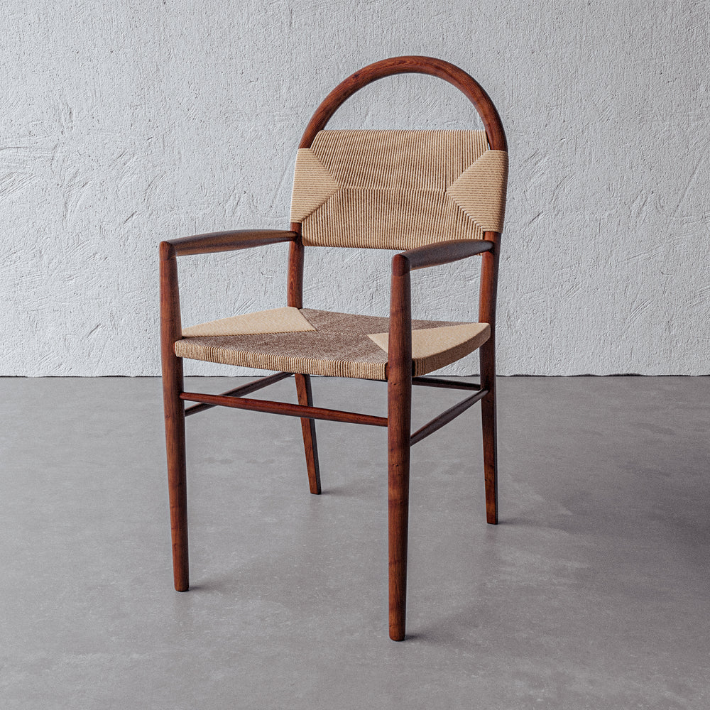 Lemieux et Cie Pernelle Dining Arm Chair, sculptural arched backrest with woven seat and arms, shown on concrete floor against white plaster wall.