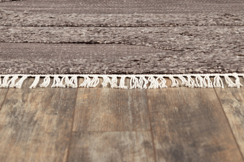 Lemieux et Cie Rafalla rug in natural gray undyed wool, handmade high-low pile with hand-knotted fringe on warm wood flooring.