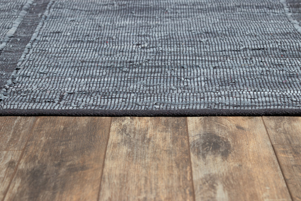 Lemieux et Cie Tézah Rug in blue and grey handwoven recycled leather, textured flat-weave shown on aged wood flooring with visible grain.