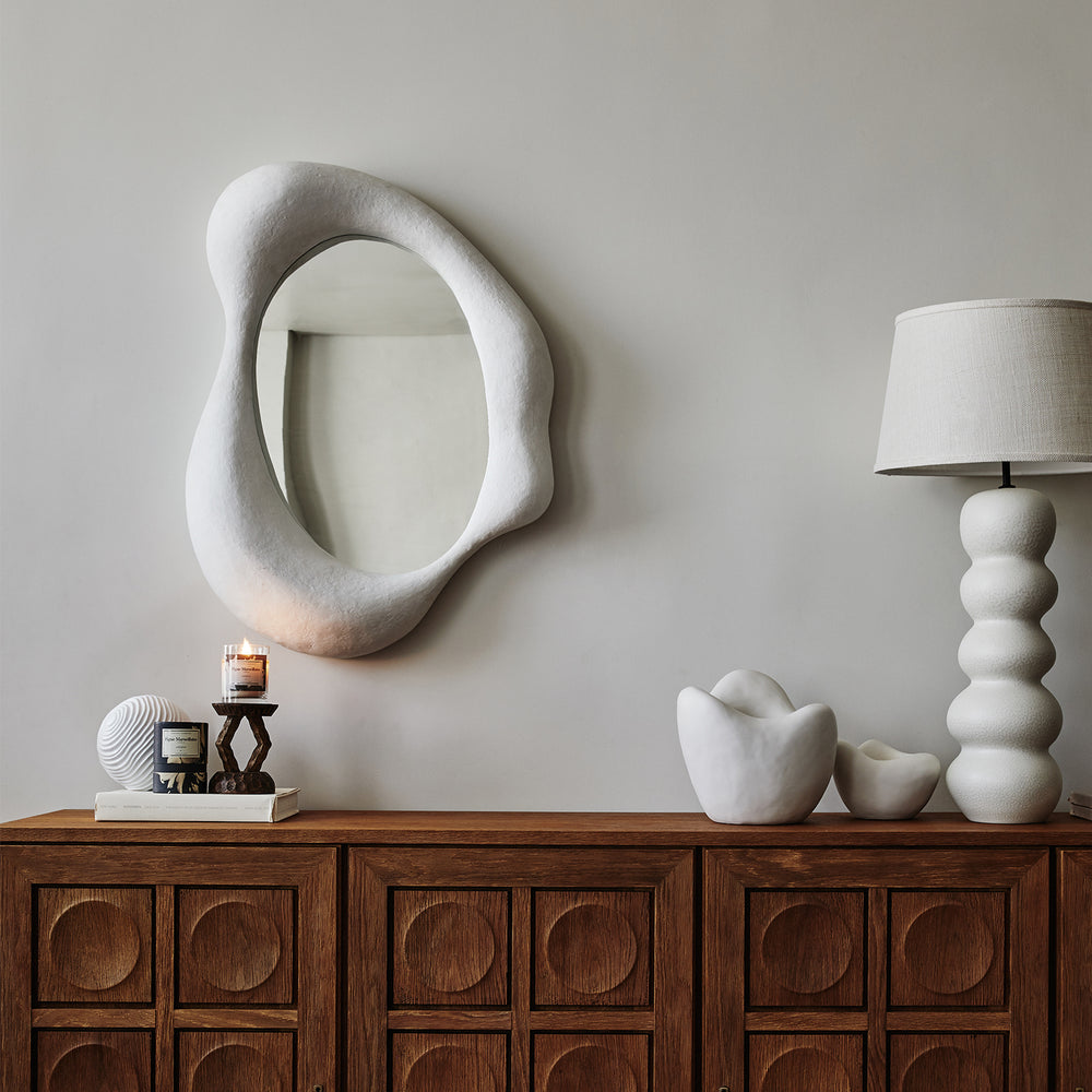 Lemieux et Cie sculptural hurricane in white, organic curved form with glass insert, styled atop wood sideboard with neutral walls and table lamp.