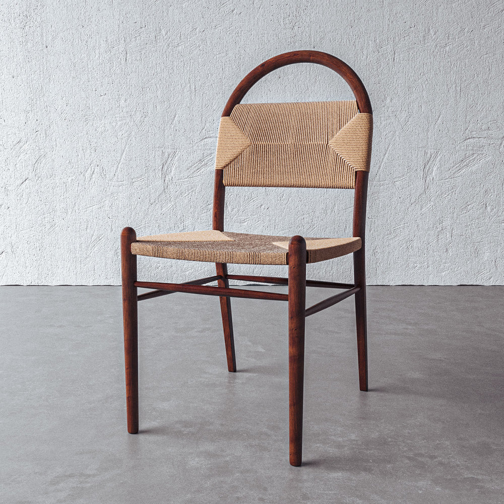 Lemieux et Cie Pernelle Dining Side Chair in walnut with woven rush seat and arched backrest, dining chair on concrete floor against textured white plaster wall.