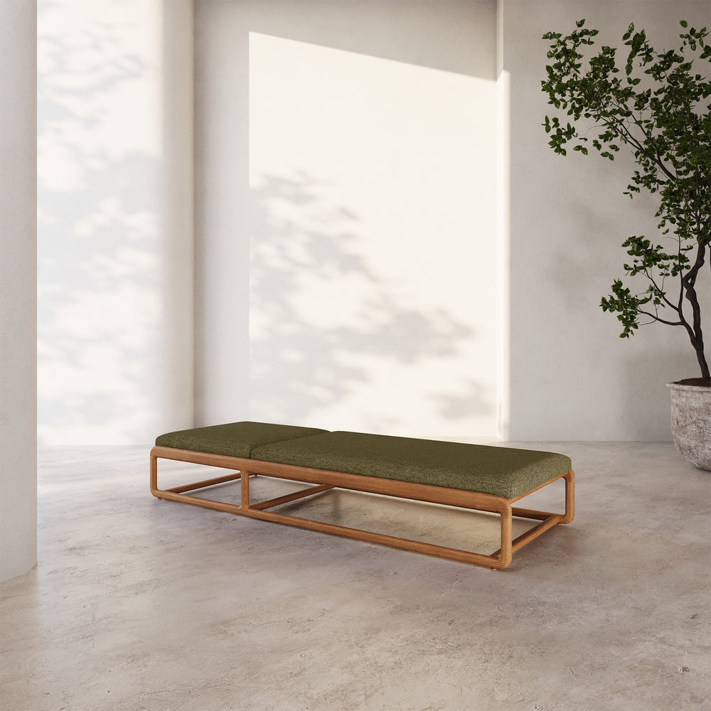 Lemieux et Cie Dock Teak Chaise Lounge with olive green cushion on sculptural teak frame, shown on concrete floor in soft daylight with white walls.