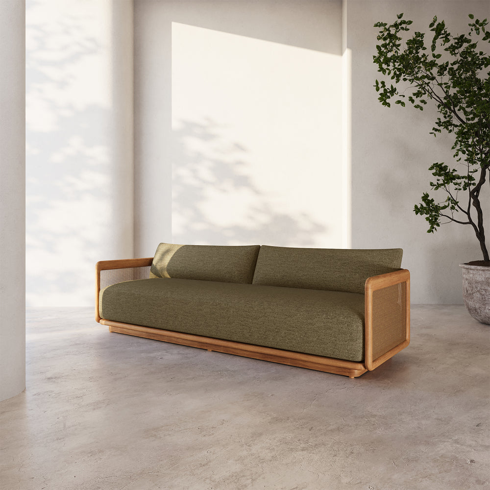 Lemieux et Cie Dock Teak 3-Seater Sofa with olive upholstery and woven teak panels, shown on stone flooring in soft daylight with white plaster walls.