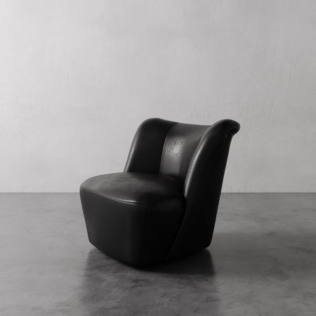 Lemieux et Cie Aurélie Leather Swivel Chair in black leather, sculptural rounded form with curved back, shown on concrete floor against white wall.