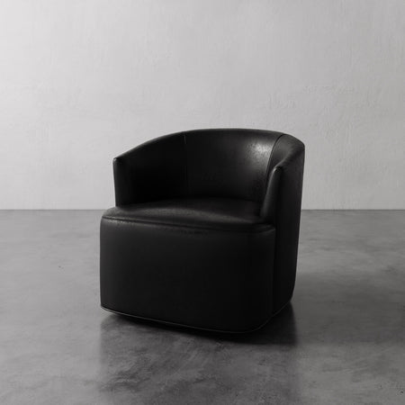Lemieux et Cie Garnier Swivel Chair in black leather, barrel-back lounge chair with rounded form, on polished concrete floor against white wall.