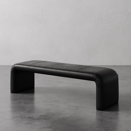 Lemieux et Cie Nadia Leather Bench in black leather, low-profile bench with rounded edges, shown on concrete floor against textured plaster walls.