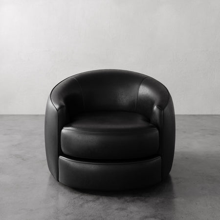 Lemieux et Cie Rulmann Swivel Chair in black leather, rounded barrel form with low profile, shown on polished concrete floor against white walls.