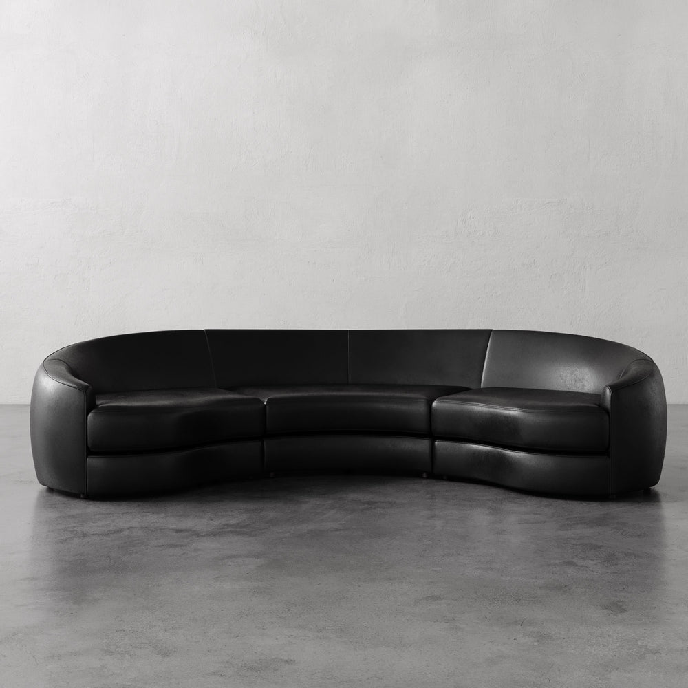 Lemieux et Cie Rulmann 3-Piece Sectional in black leather, curved modular sofa on polished concrete floors with neutral plaster walls.