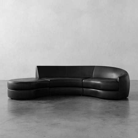 Lemieux et Cie Rulmann Right Sectional in black leather, curved three-piece sofa with rounded forms, shown on concrete floor against white walls.