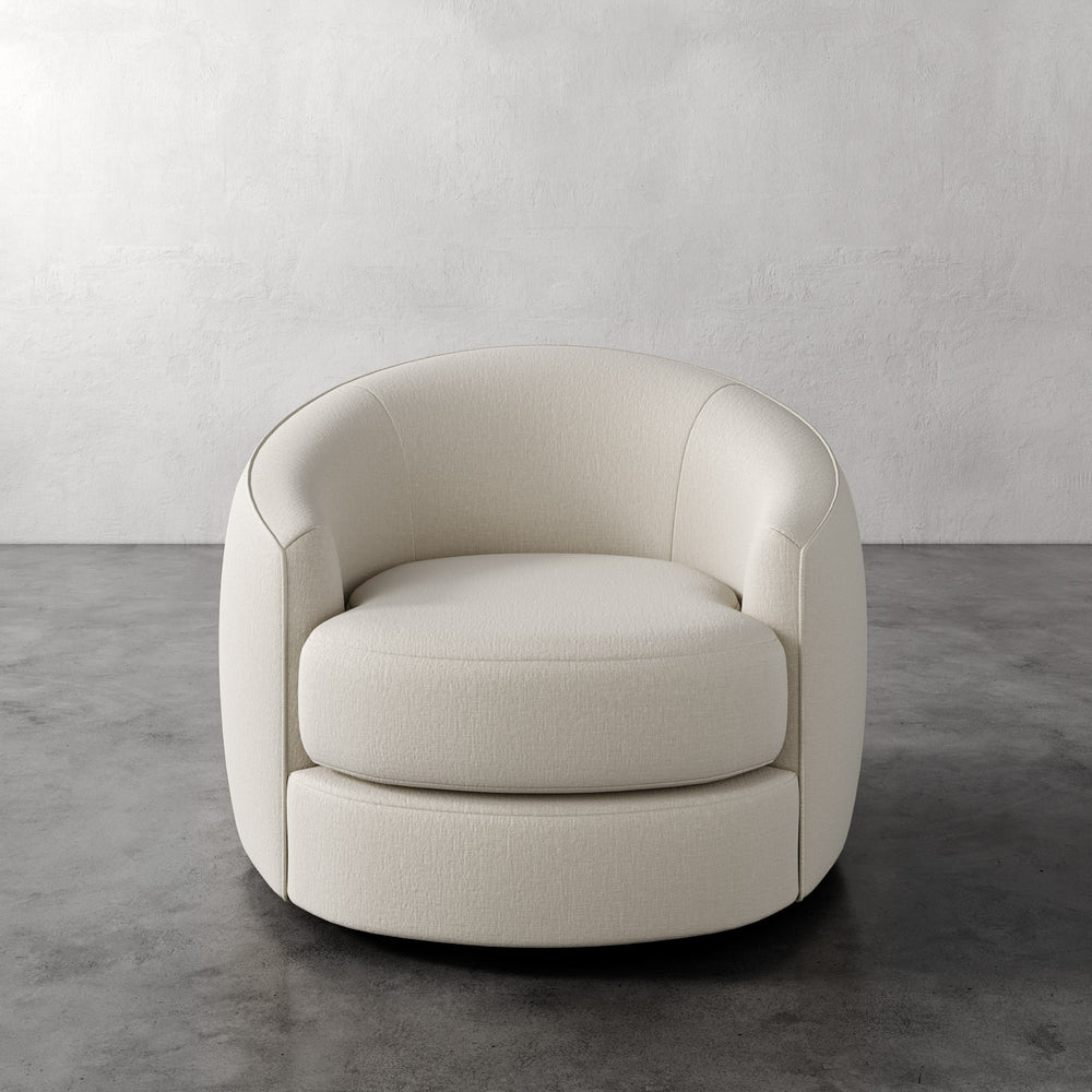 Lemieux et Cie Rulmann Swivel Chair in ivory, rounded barrel-back lounge chair on polished concrete floor with textured plaster walls.