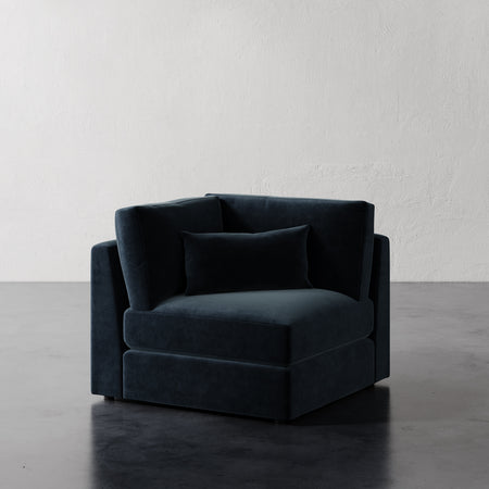 Lemieux et Cie Lacroix Corner Chair in charcoal upholstery, modular seating with rectilinear form and bolster pillow, on dark polished floor against white plaster walls.