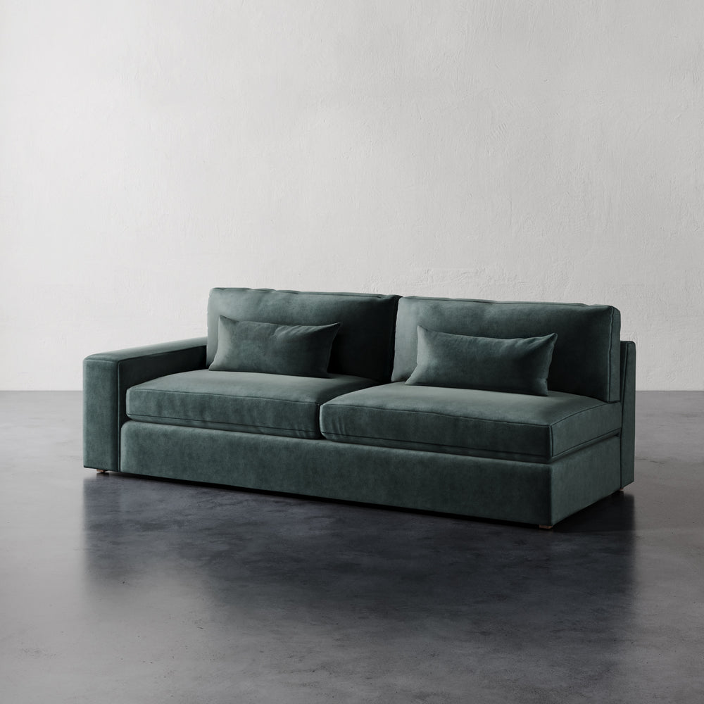 Lemieux et Cie Lacroix Left Arm Sofa in deep teal upholstery, modular sofa with bolster pillows on dark concrete floor against neutral walls.