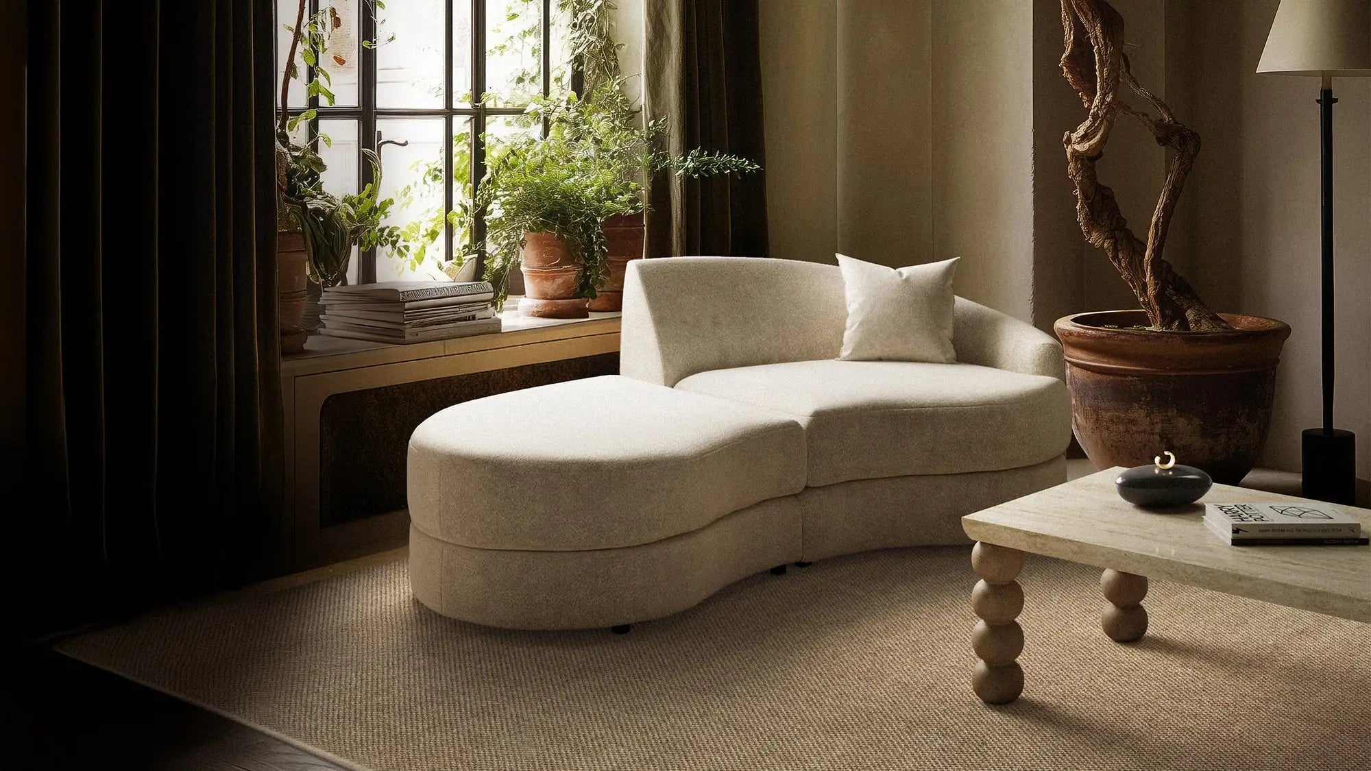 Beige chaise lounge in a living room with plants and a lamp.