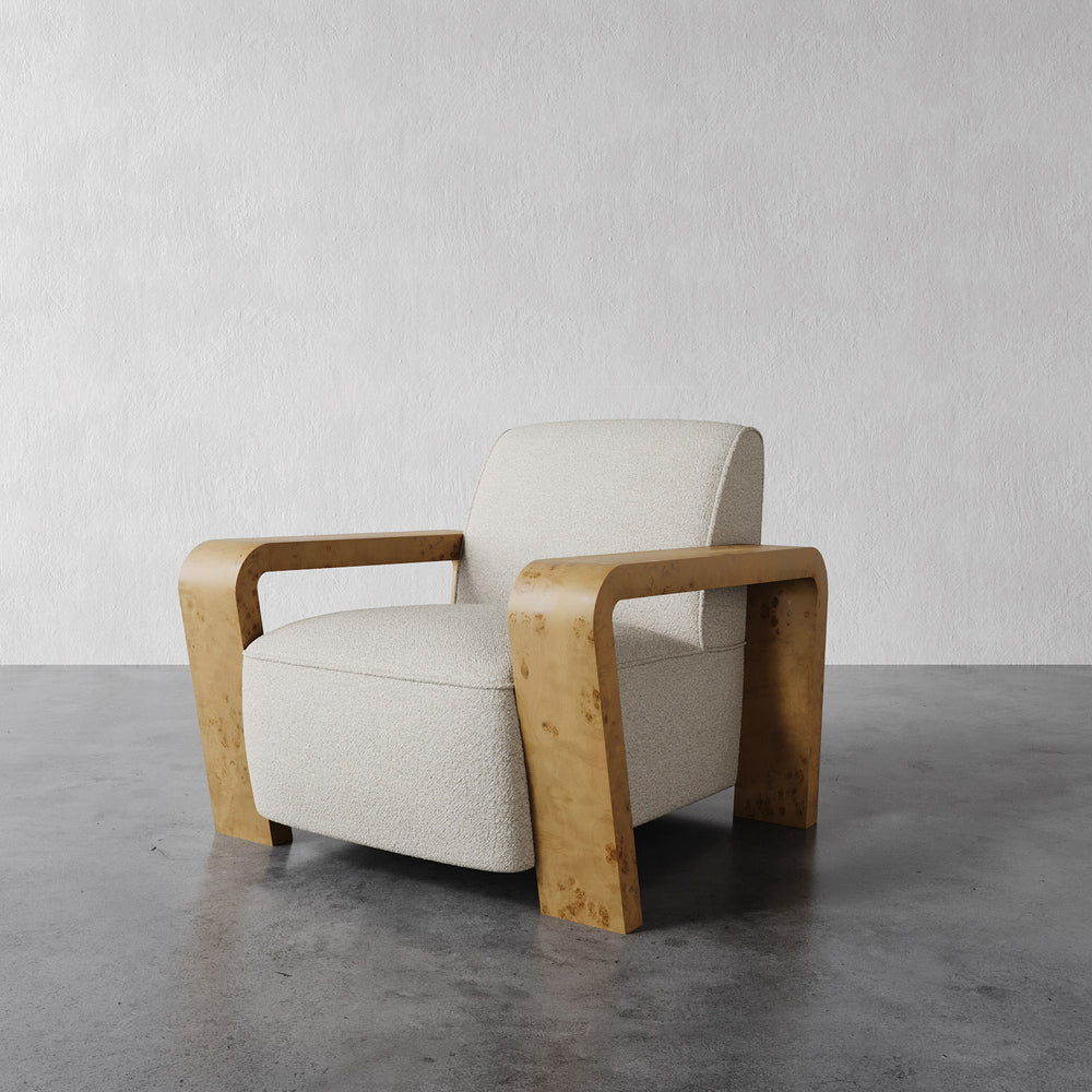 Lemieux et Cie Dumas Lounge Chair with sculptural curved armrests and ivory upholstery, shown on polished concrete floor against textured plaster walls.