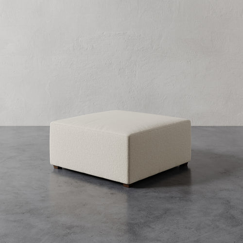 Lemieux et Cie Fabien 36" Square Ottoman in neutral upholstery, low-profile ottoman shown on concrete floor against textured plaster walls.