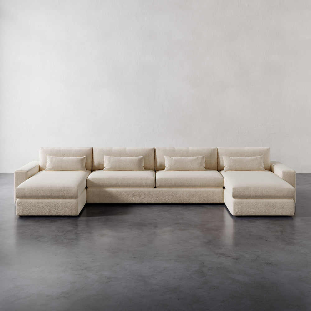 Lemieux et Cie Lacroix Sofa in ivory, low-profile U-sectional with dual chaises and four cushions, on concrete floor against plaster walls.
