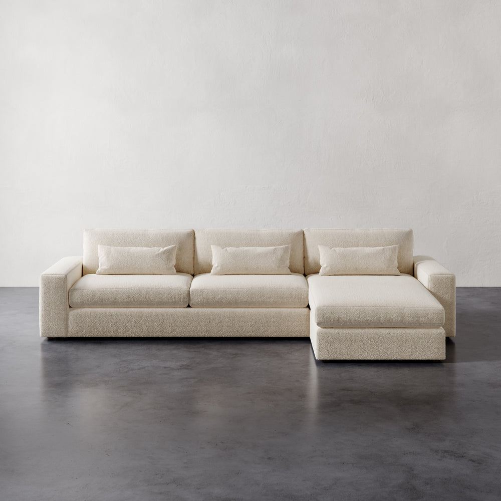 Lemieux et Cie Lacroix Right Chaise Sectional in ivory bouclé, modular sofa with deep cushions and bolsters, on dark concrete floor with neutral plaster walls.