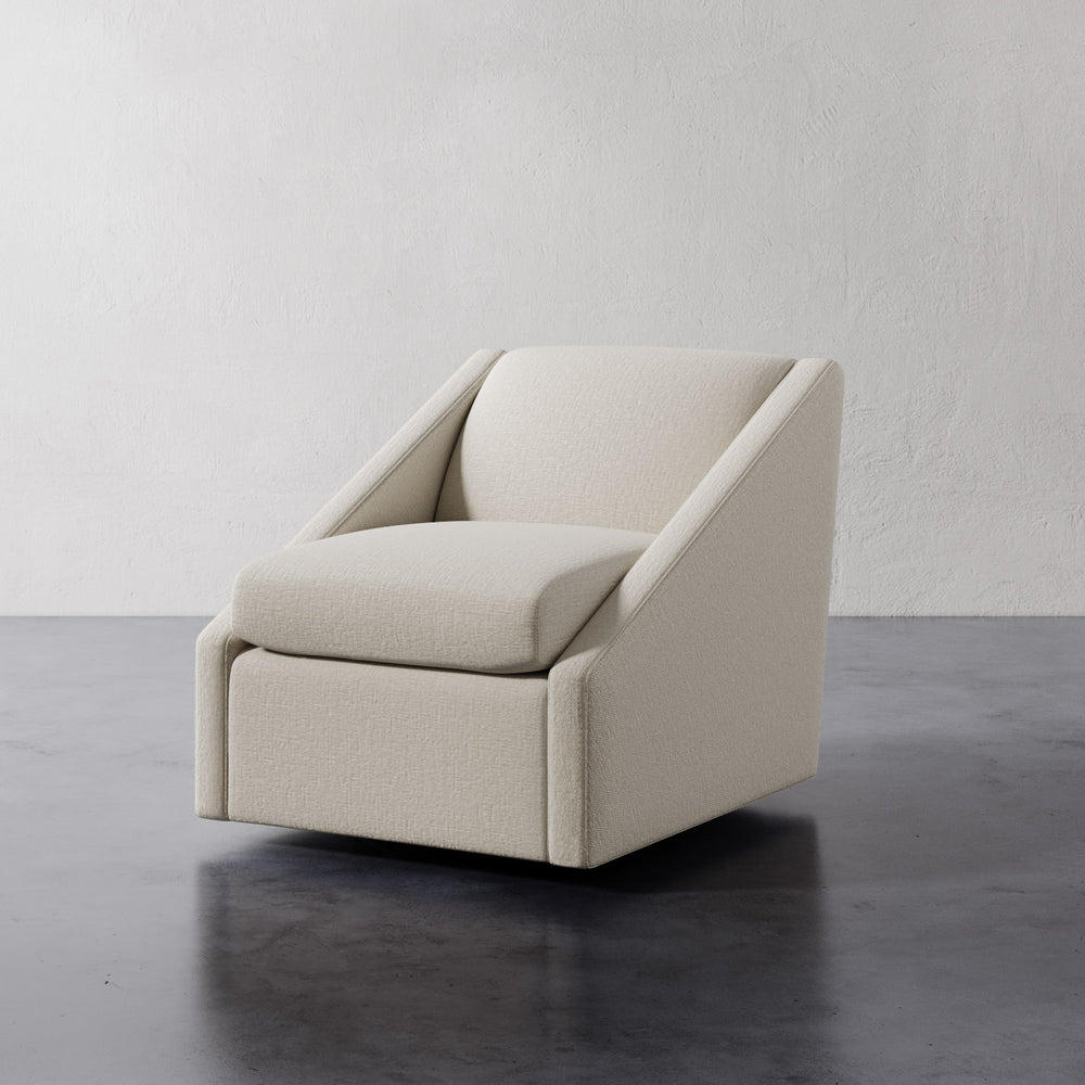 Lemieux et Cie Fontaine Swivel Chair in ivory upholstery, sculptural lounge chair with angular silhouette, shown on dark concrete floor against textured plaster walls.