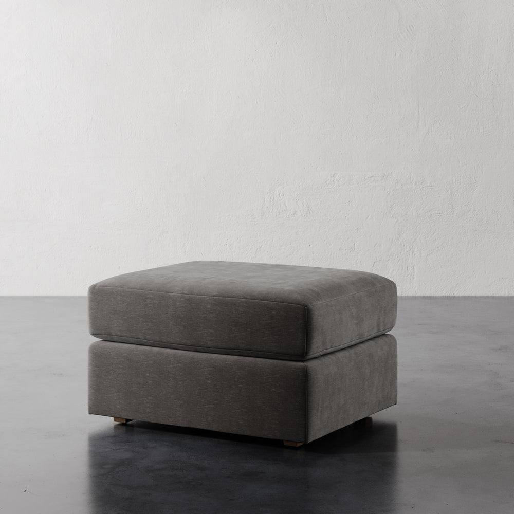 Lemieux et Cie Lacroix Ottoman, low-profile upholstered ottoman with clean rectilinear form, shown on concrete floor against textured white plaster wall.