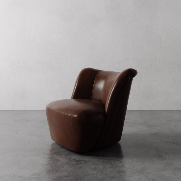 Lemieux et Cie Aurélie Leather Swivel Chair in warm brown leather, sculptural rounded form on concrete floor against plaster walls.