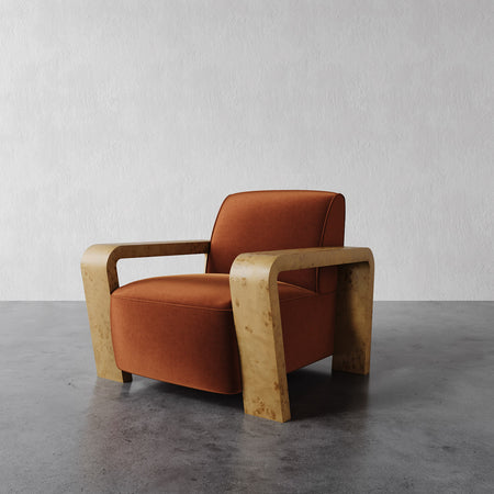Lemieux et Cie Dumas Lounge Chair with rounded arms and warm rust upholstery, shown on polished concrete floor against textured white wall.