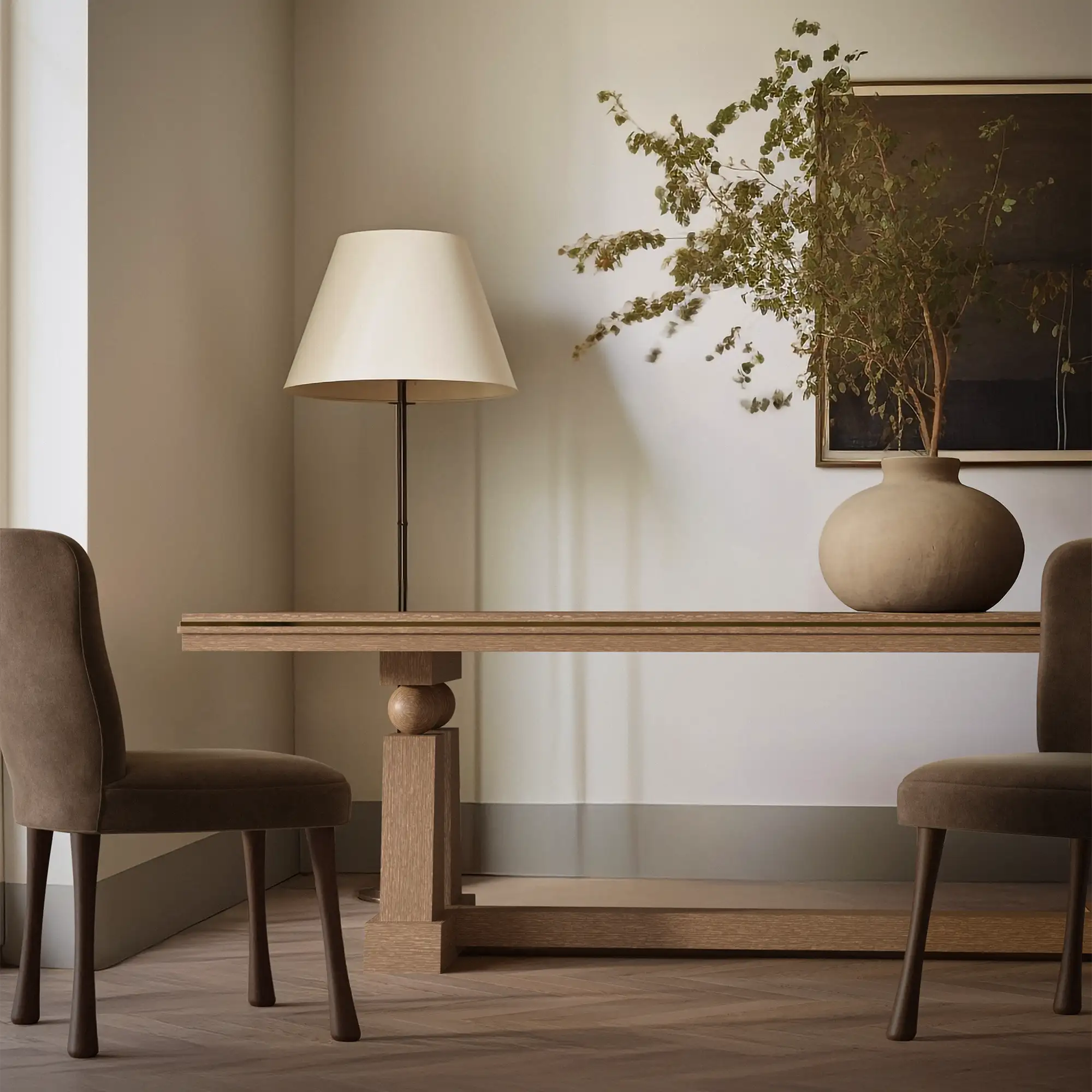 Lemieux et Cie Corvaux Dining Table, sculptural turned pedestal base with trestle support, styled with table lamp and vase in neutral dining room with wood flooring.